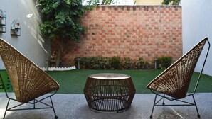 Two wicker chairs and a round table in an outdoor patio area with a brick wall and greenery in the background. - Valentin House, very spacious and cozy. (San Luis Potosí)