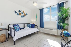 Un dormitorio con cama, ventana con cortinas, radiador, planta en maceta y decoración en la pared.