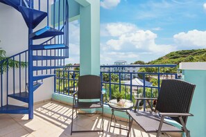 Un balcon agrémenté d’un escalier en colimaçon bleu, de deux fauteuils en osier et d’une petite table sur laquelle est posée une plante en pot.