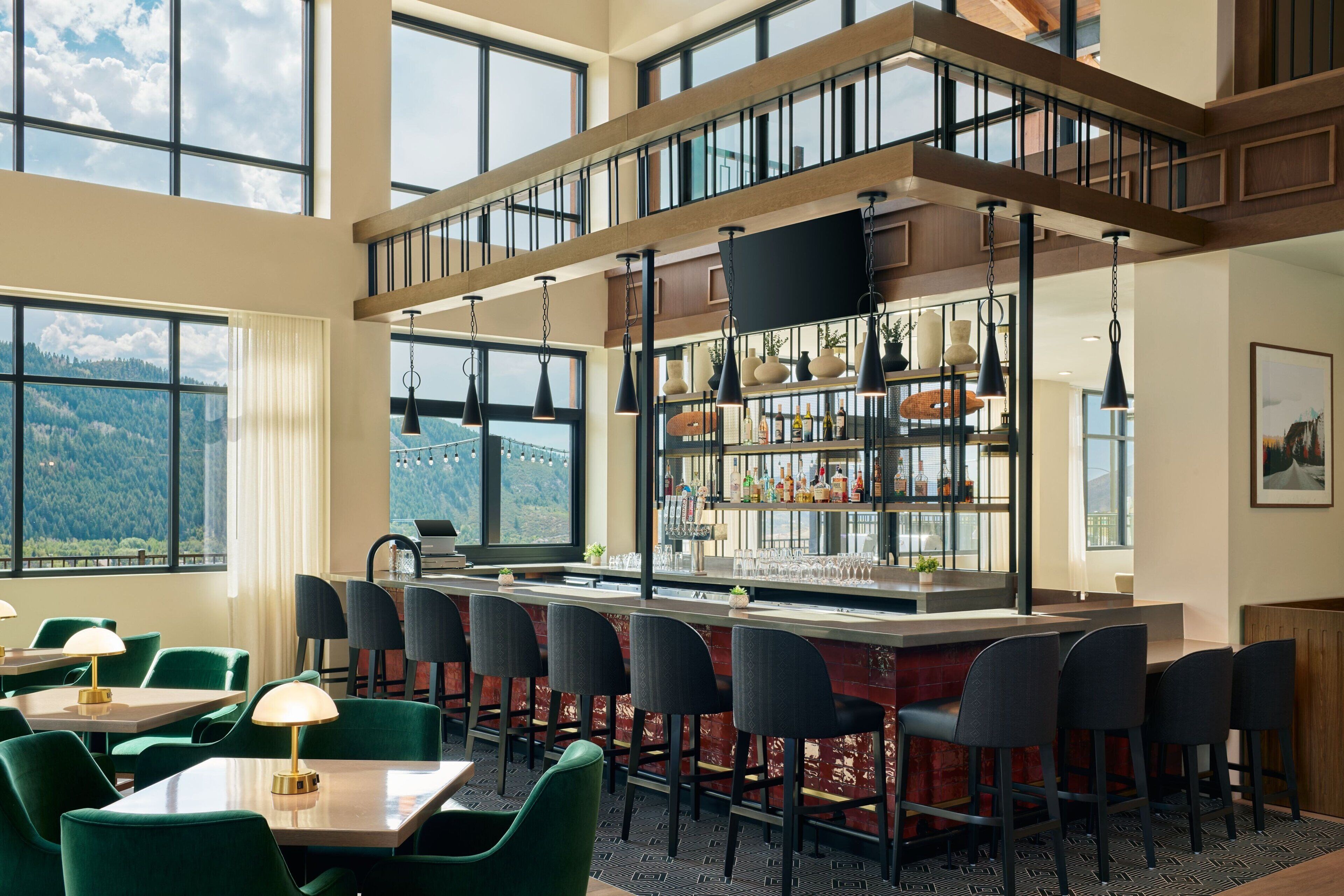 A high-ceiling bar area with multiple seating options, a large window offering a mountain view, and a modern interior design.