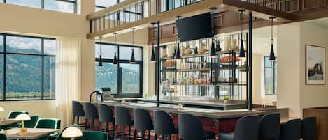 A high-ceiling bar area with multiple seating options, a large window offering a mountain view, and a modern interior design.