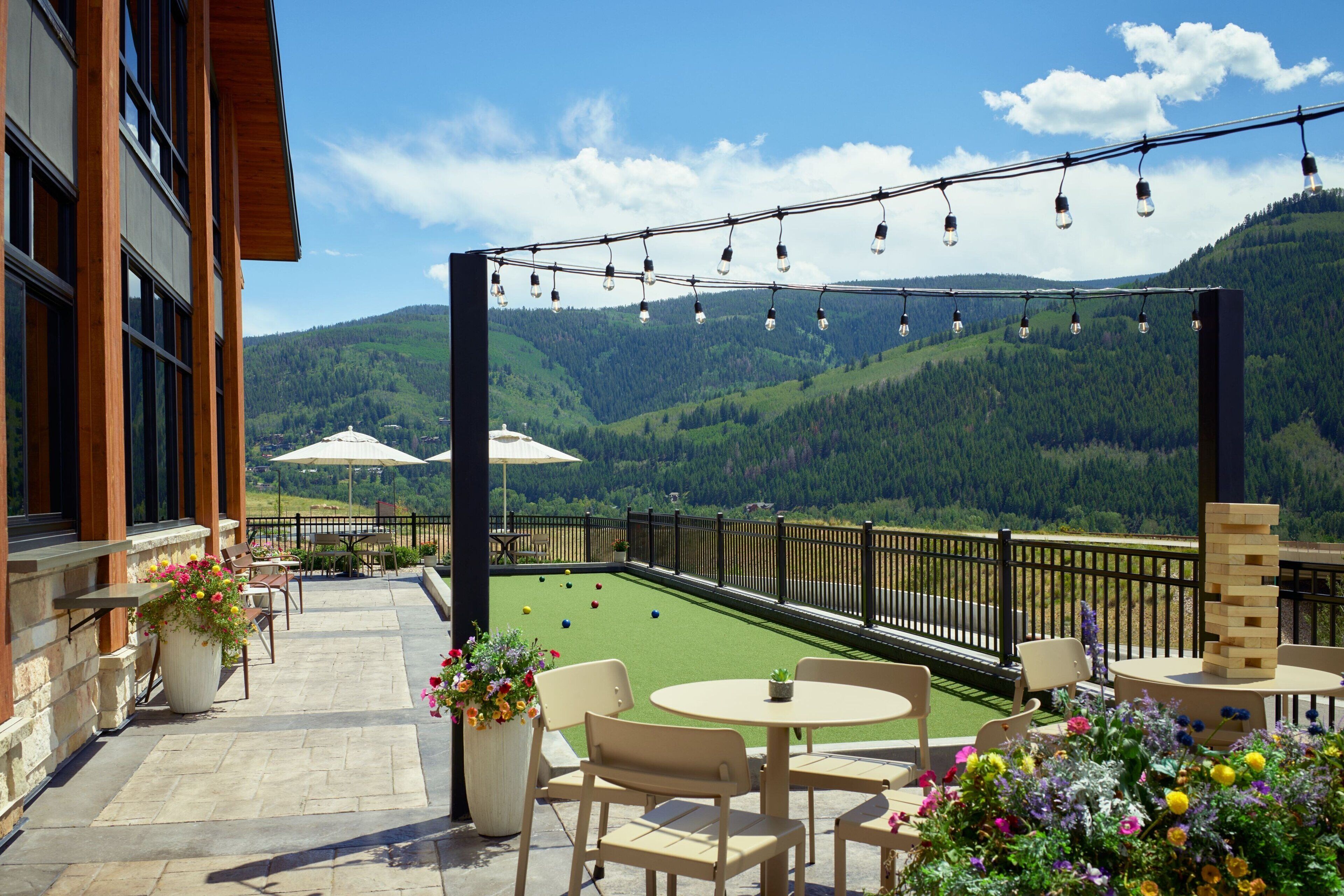 Una terraza con asientos al aire libre, un campo de croquet y una vista panorámica de las montañas.