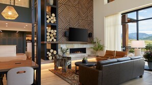 A modern living room with a fireplace, comfortable seating, and a large window offering a view of the outdoors. - SpringHill Suites by Marriott Avon Vail Valley (Avon)