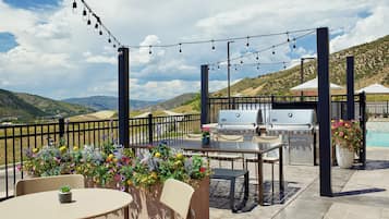 An outdoor patio with a grill, seating, string lights, and flower planters.