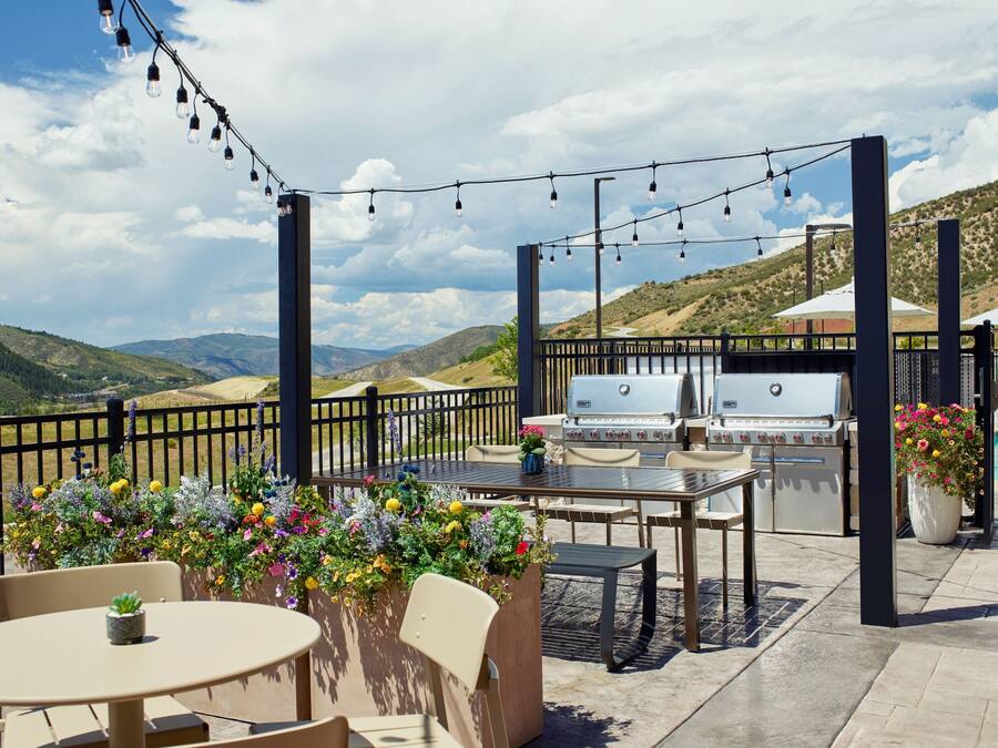 An outdoor patio with a grill, seating, string lights, and flower planters.
