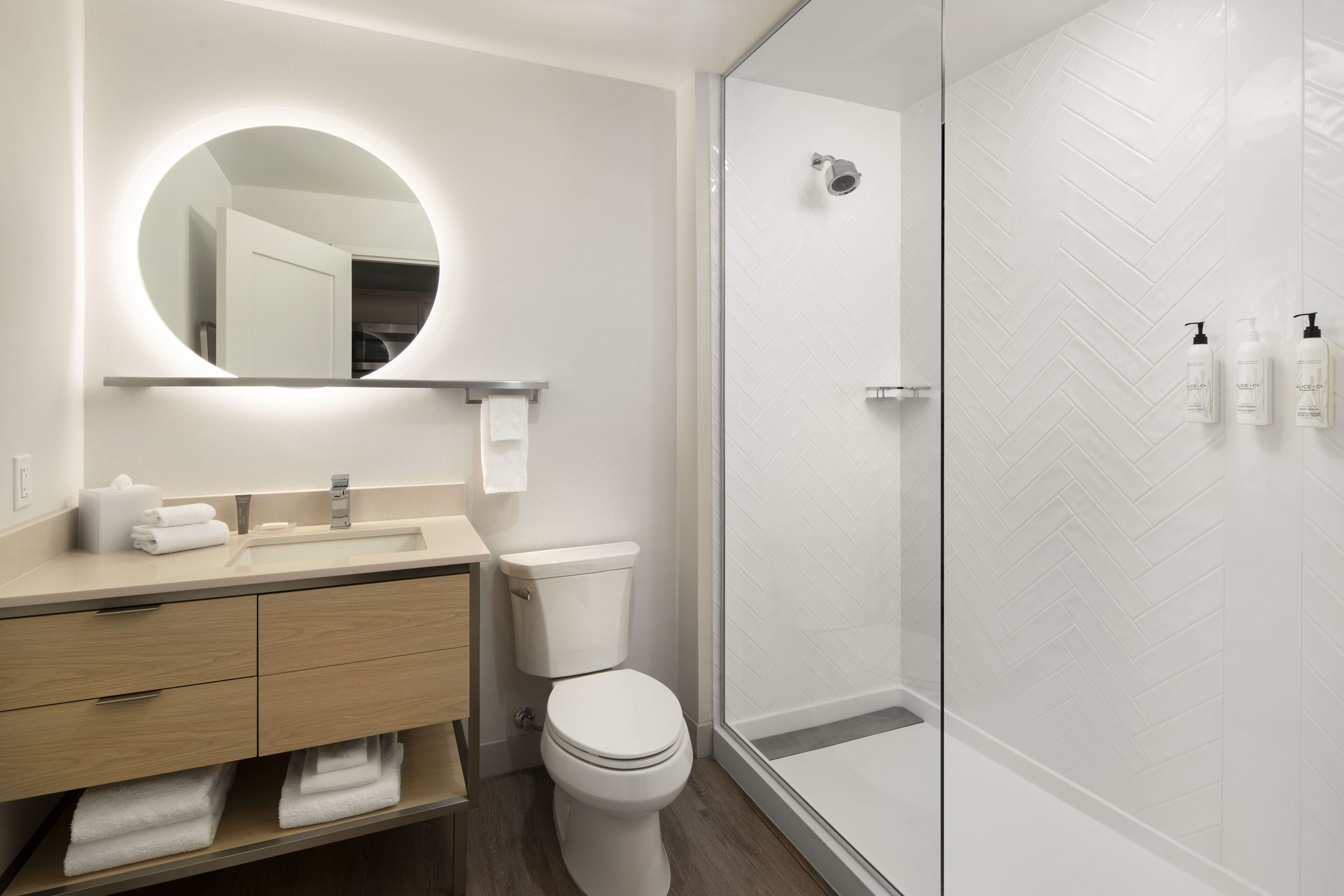 Ein modernes Badezimmer mit rundem Spiegel, Waschbecken, Toilette und Duschbereich.