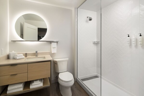Un baño moderno con un espejo redondo, un lavabo, un inodoro y una zona de ducha.