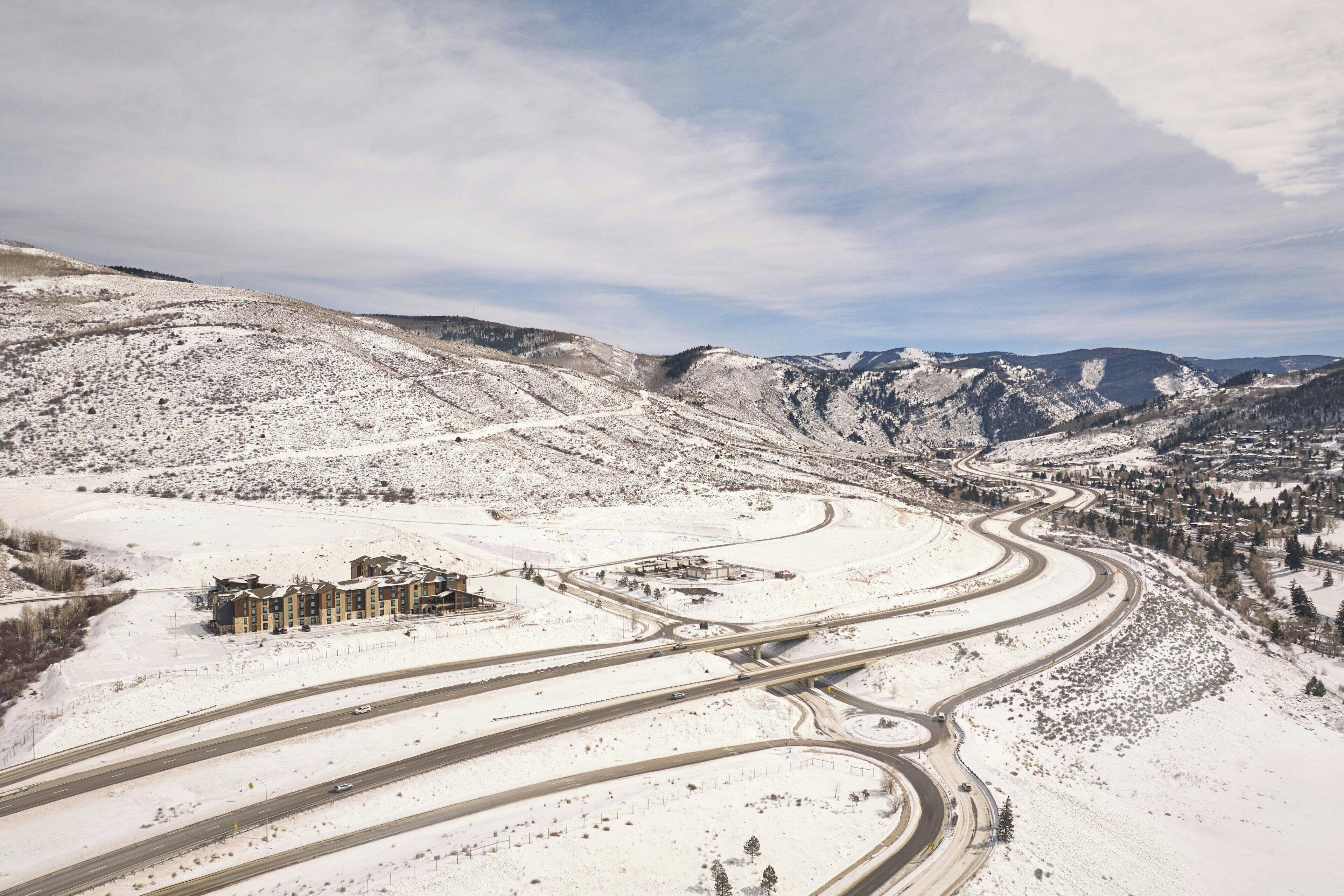 Zona montañosa cubierta de nieve, con una autopista de varios carriles y un conjunto de edificios.