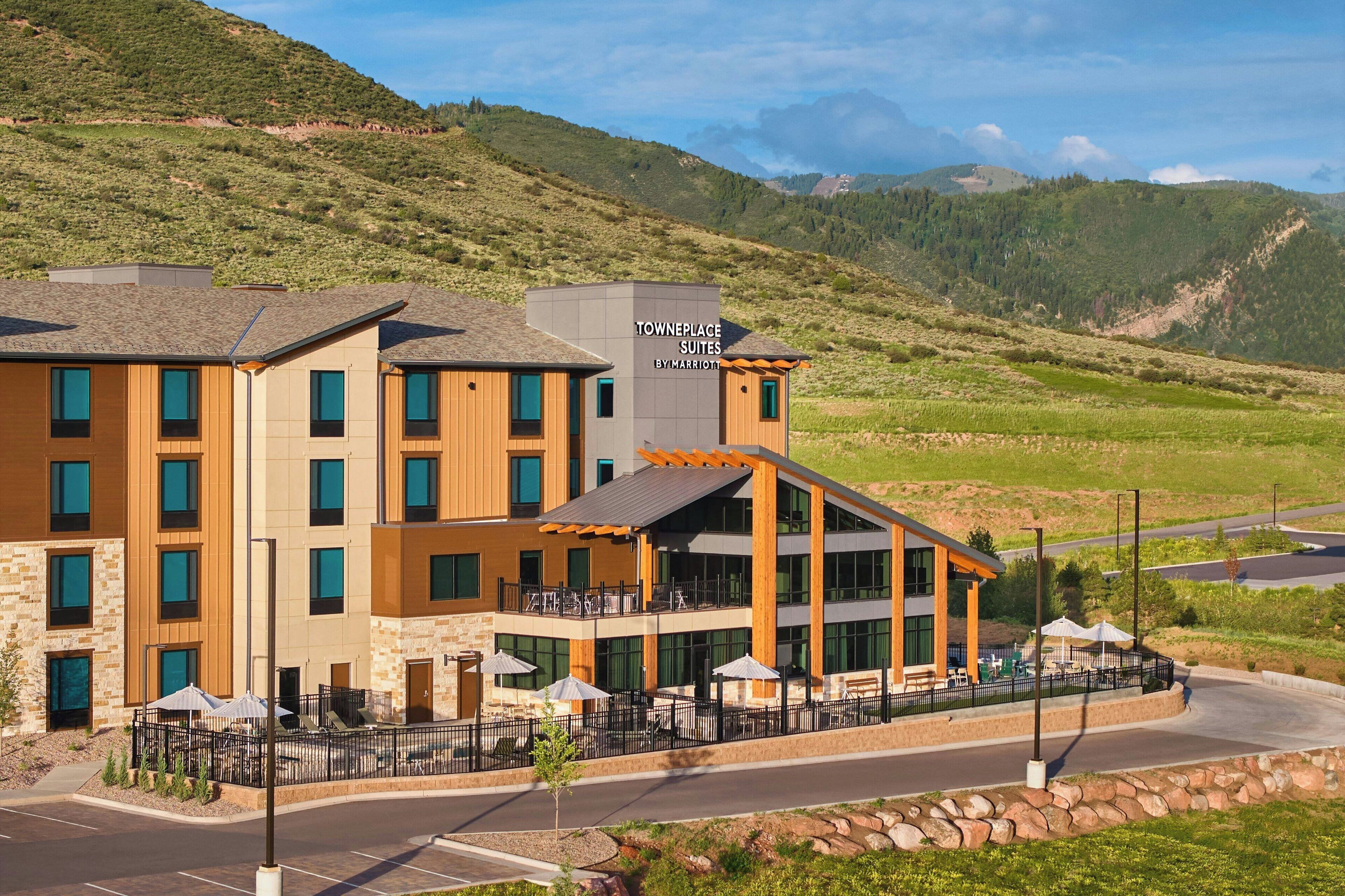 A modern hotel with a sign reading "TOWNEPLACE SUITES BY MARITON" in a hilly area.