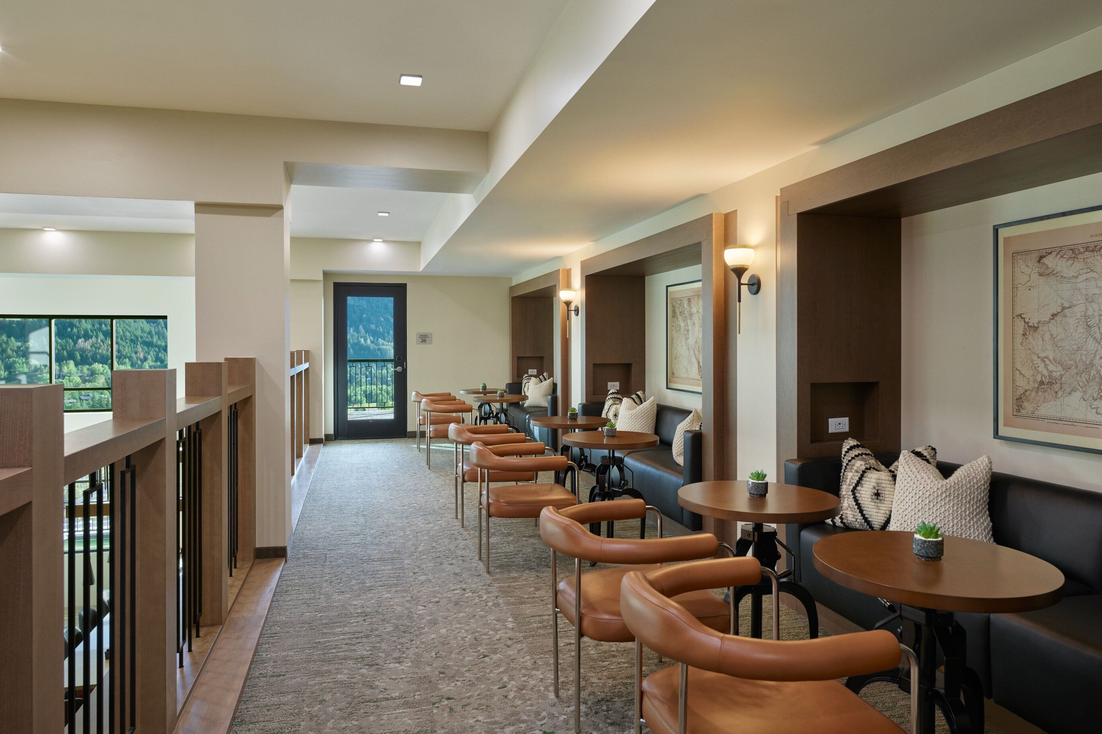 A hotel lobby with a long corridor lined with brown leather chairs and round tables, a black leather sofa, and a large framed map on the wall.