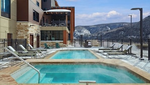 Une piscine sur le toit, divisée en deux espaces distincts, entourée de chaises longues et dotée d’un bar offrant une vue sur les montagnes enneigées.