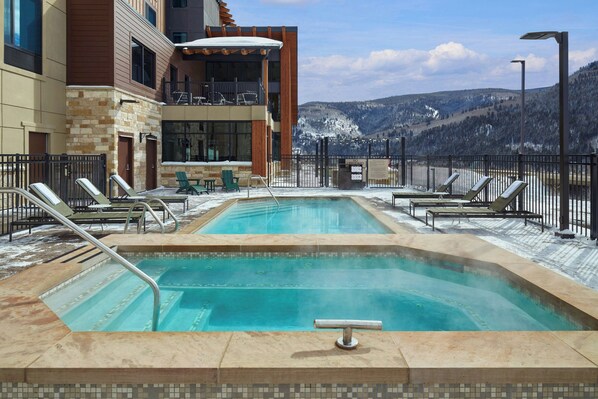 Piscina en la azotea con dos zonas separadas, rodeada de sillones de descanso y una zona de bar con vistas a montañas nevadas.