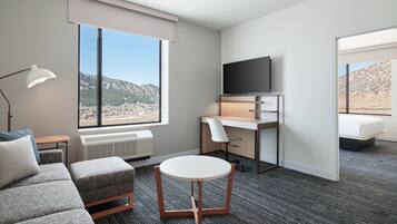 Una habitación de hotel moderna con un ventanal grande, un televisor de pantalla plana, un escritorio, un sofá y una mesa redonda.
