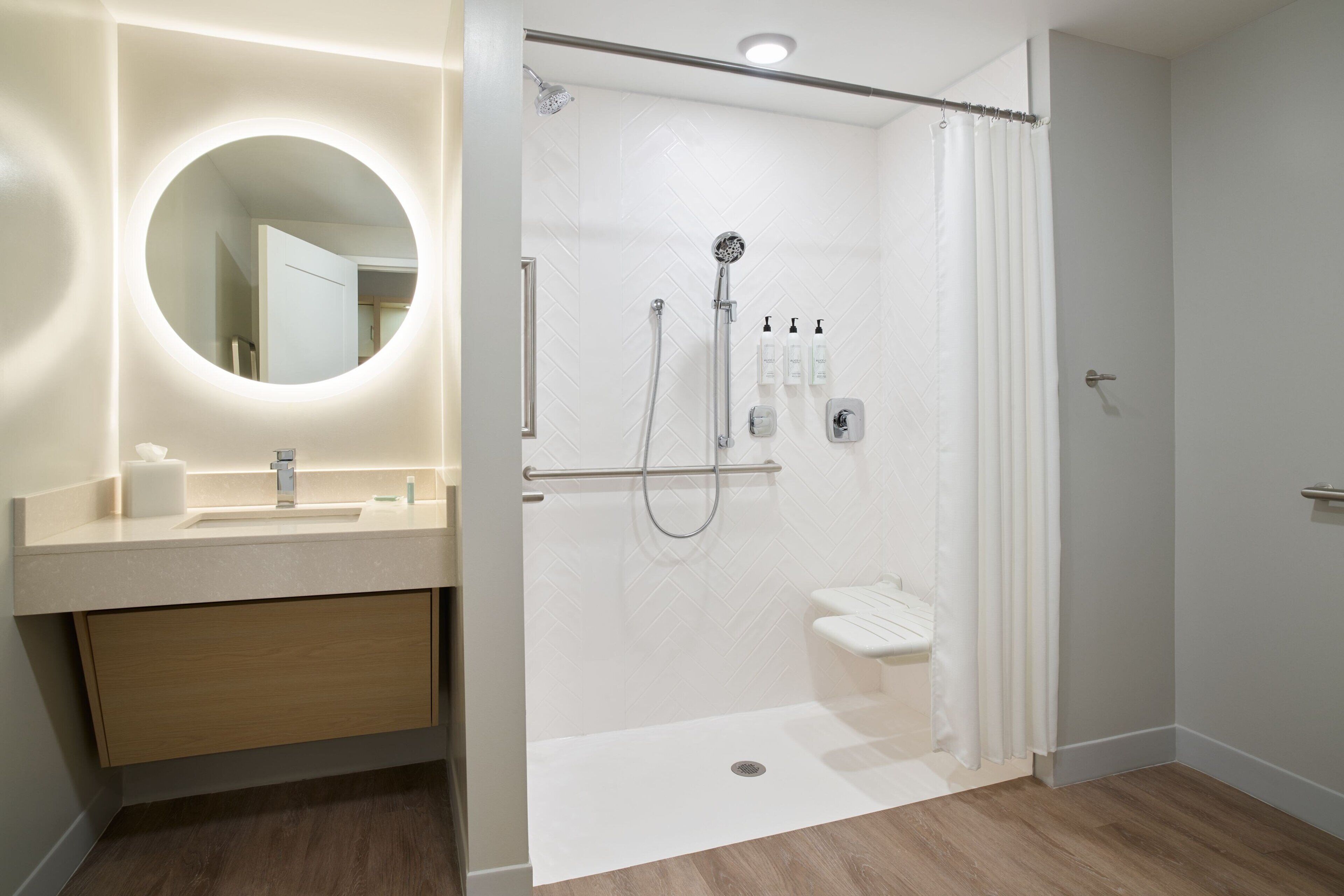 Een moderne badkamer met een glazen douchecabine, een ronde spiegel en een houten wastafelmeubel.
