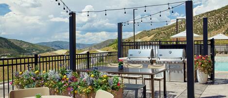 An outdoor patio with a grill, seating, and string lights.