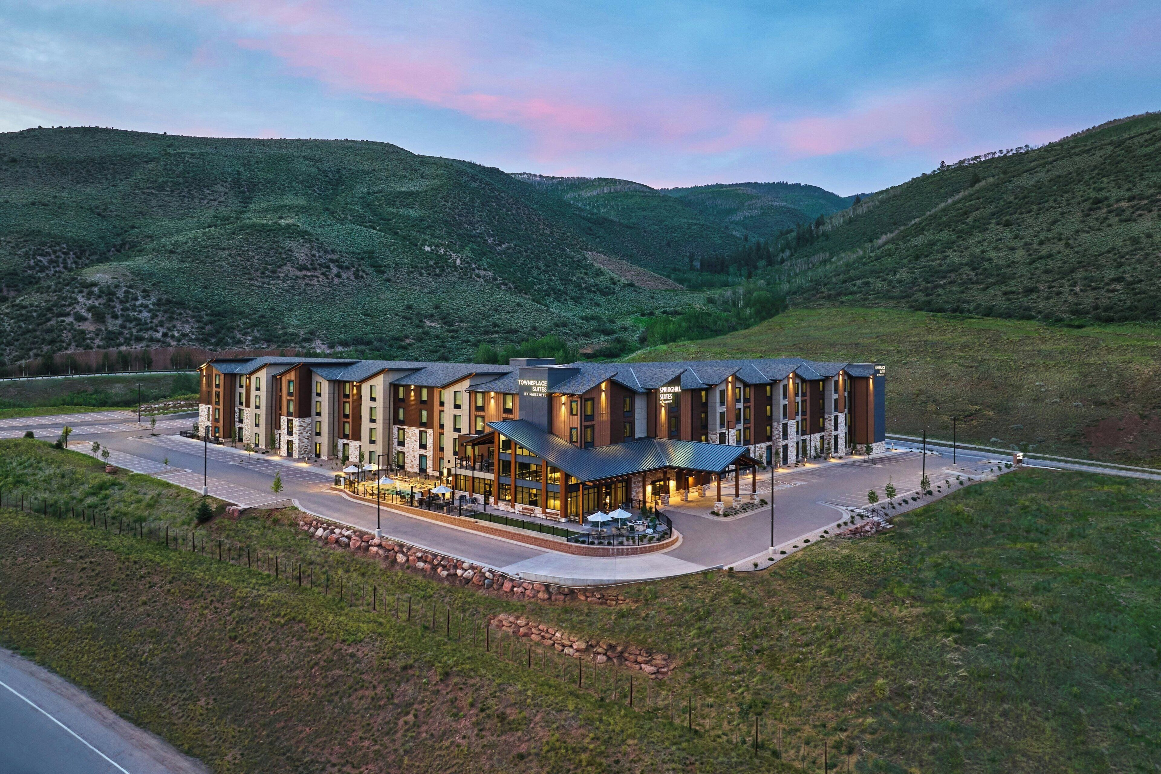 Et moderne hotel med flere bygninger, en central gårdsplads og en naturskøn bjergbaggrund.