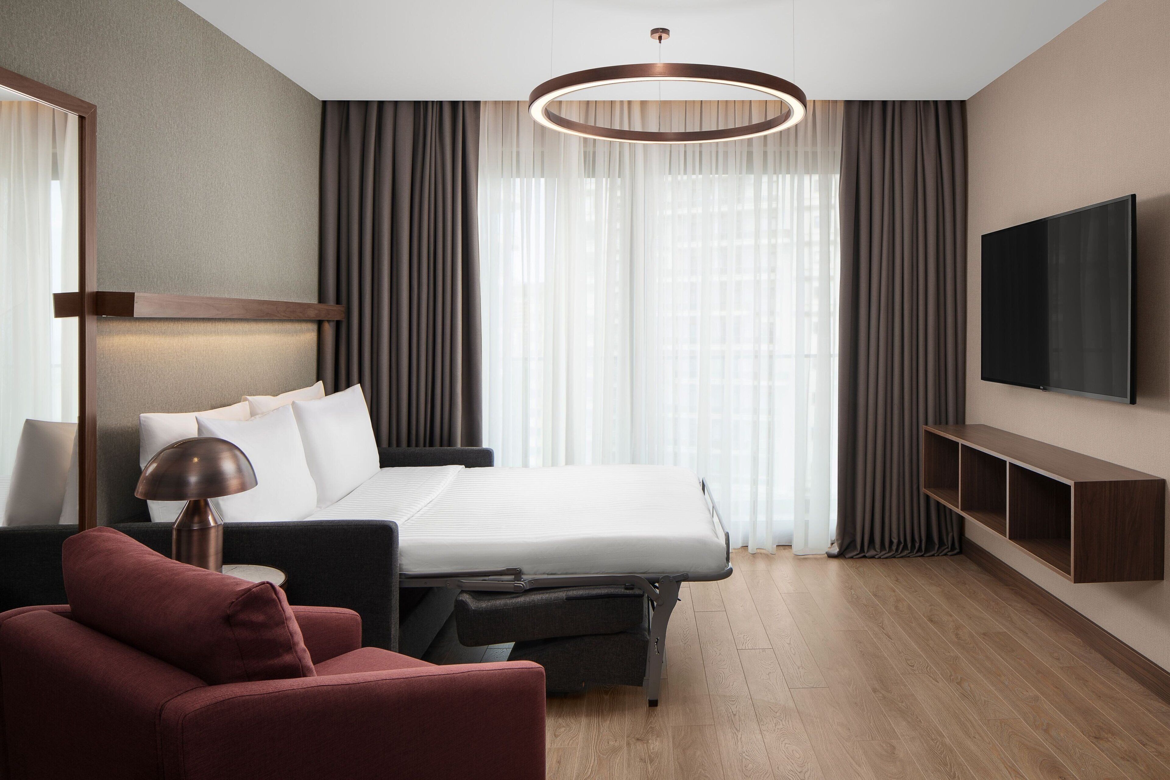 A modern hotel room with a large bed, a flat-screen TV, a desk, and a chair.