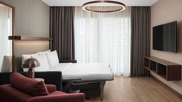 A modern hotel room with a large bed, a flat-screen TV, a desk, and a chair.