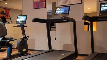 Academia com esteiras, bicicleta ergométrica e uma tela digital mostrando opções de treino.