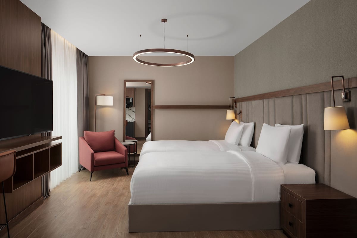 A modern hotel room with a large bed, a TV, a desk, and a chair.