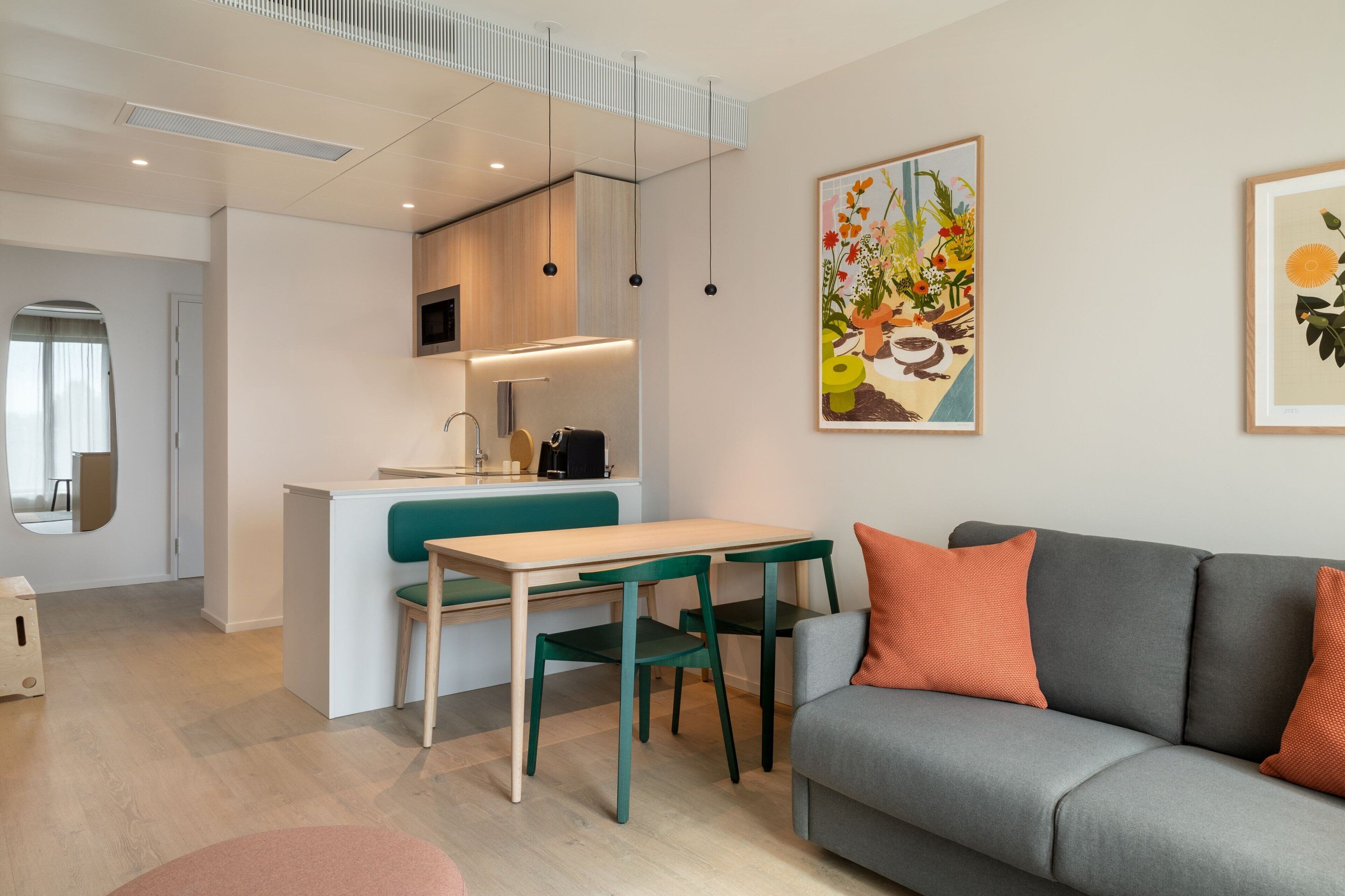 Een moderne woonruimte met keuken, eethoek en een grijze bank met oranje kussens.