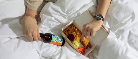 A person lying on a bed with a box of food and a bottle.