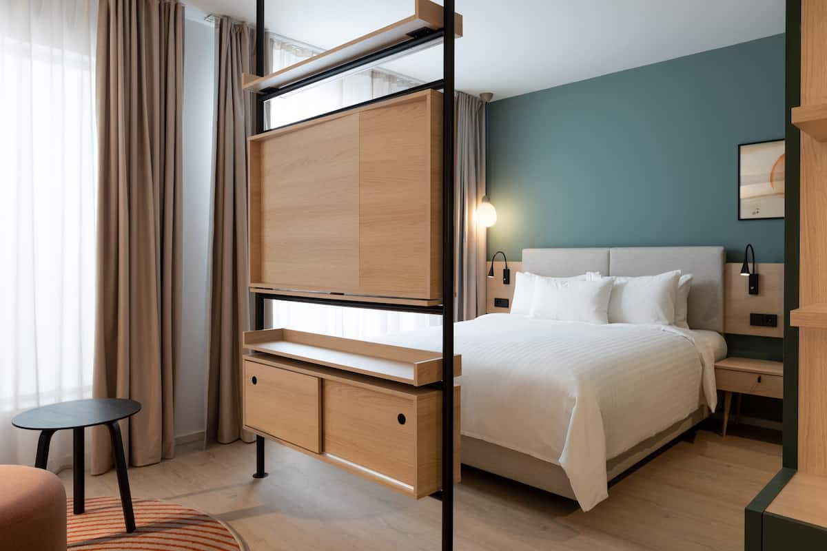 A modern hotel room with a bed, bedside tables, a desk, and a chair.