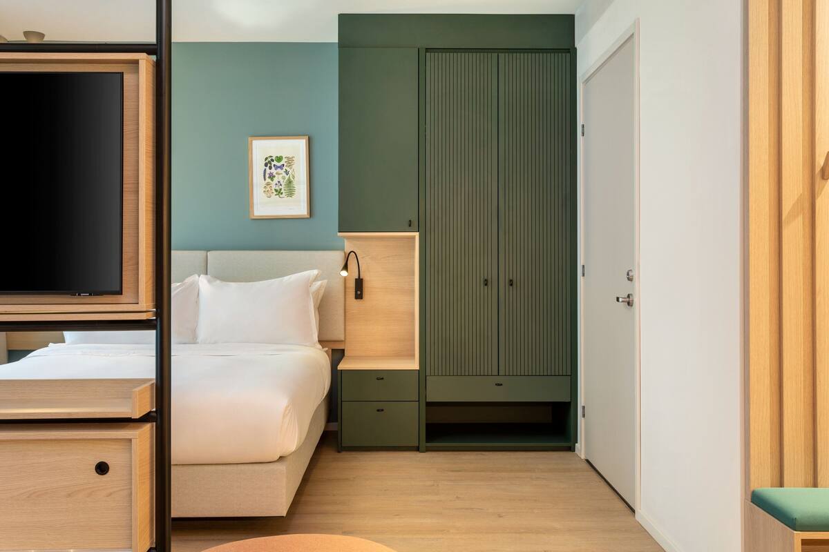 A bedroom with a bed, bedside table, TV, wardrobe, and a framed picture on the wall.