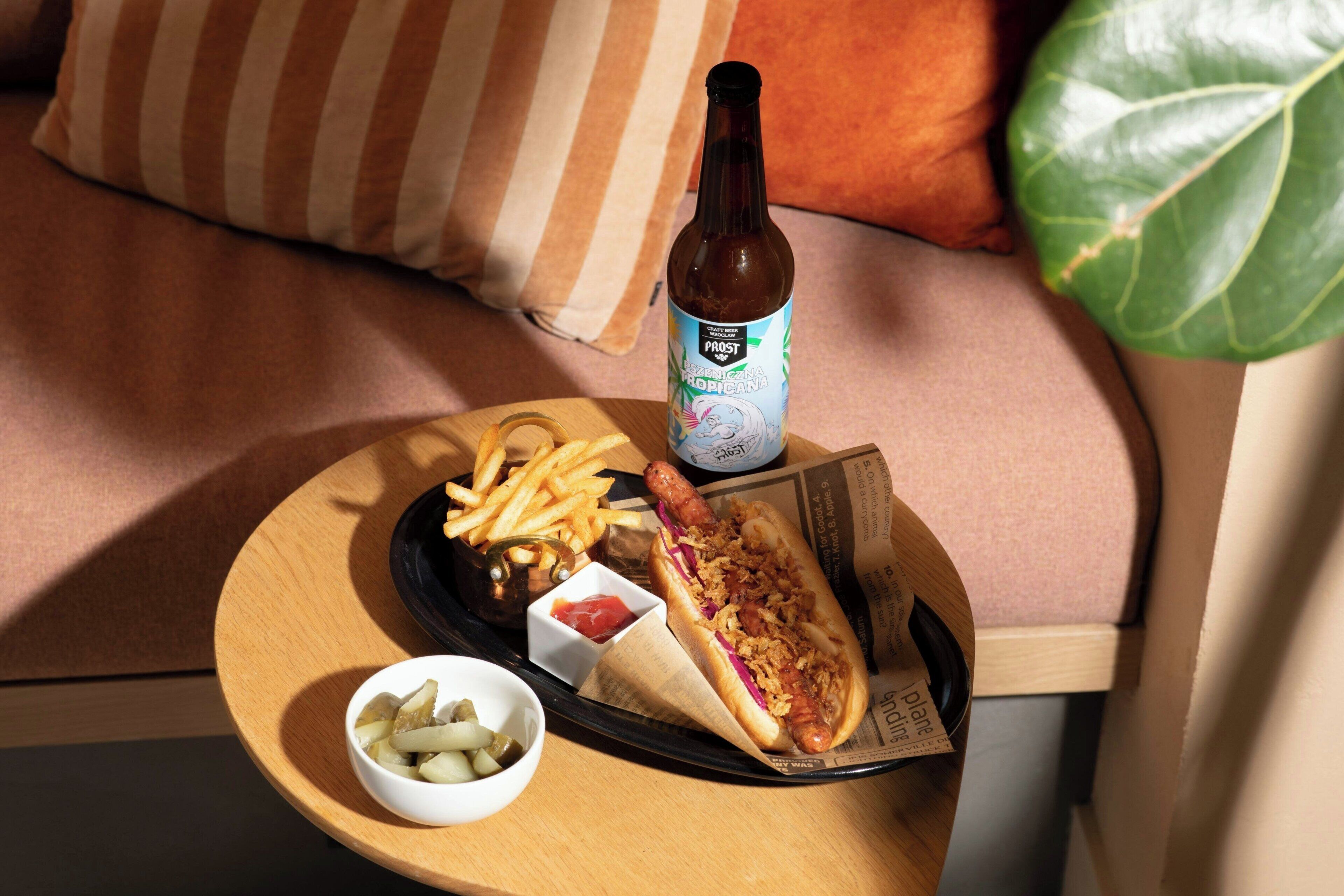 A meal tray with a hot dog, fries, and pickles on a wooden table.