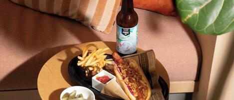 A meal tray with a hot dog, fries, and pickles on a wooden table.