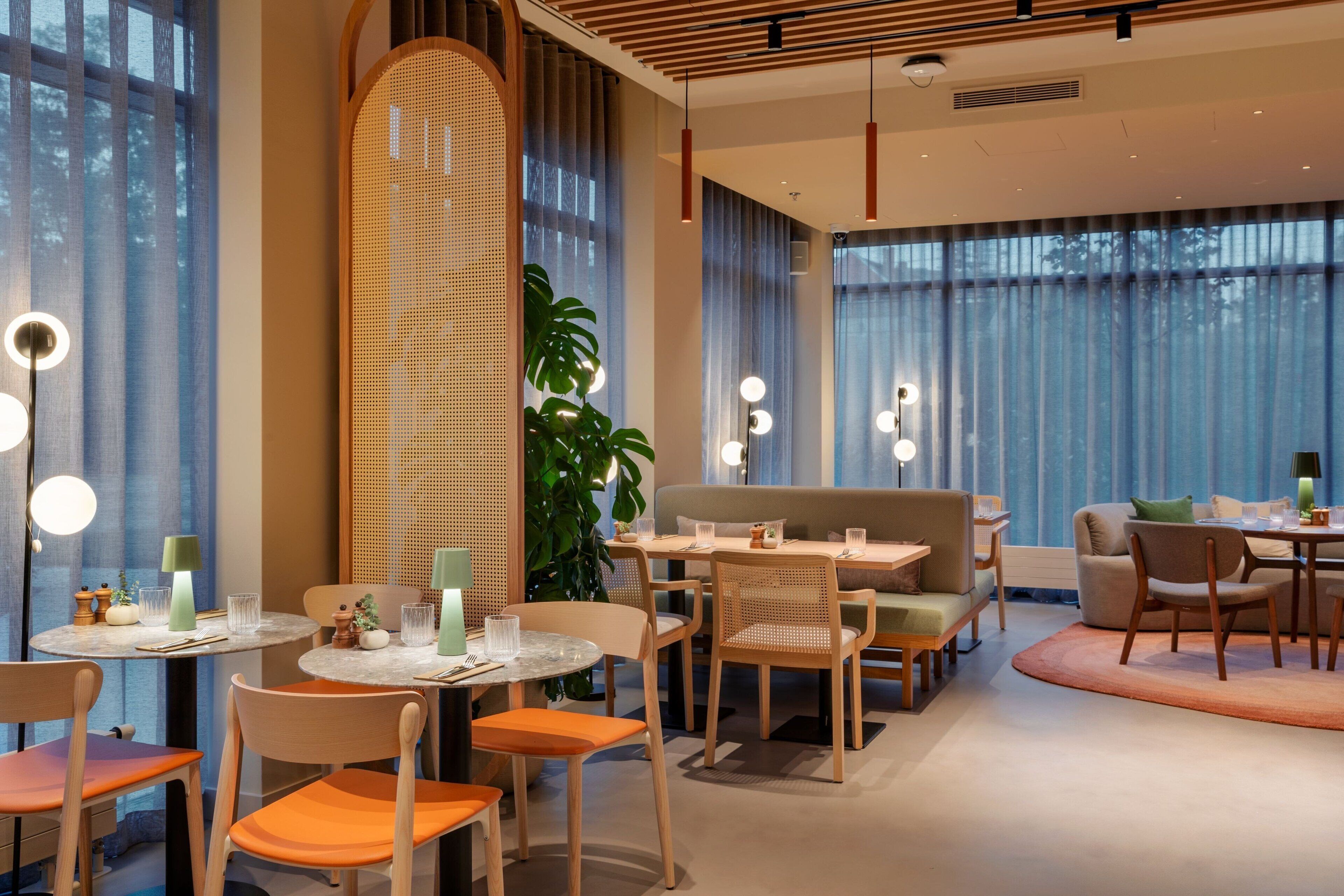 Een moderne eetruimte met ronde tafels, houten stoelen en sfeerverlichting.
