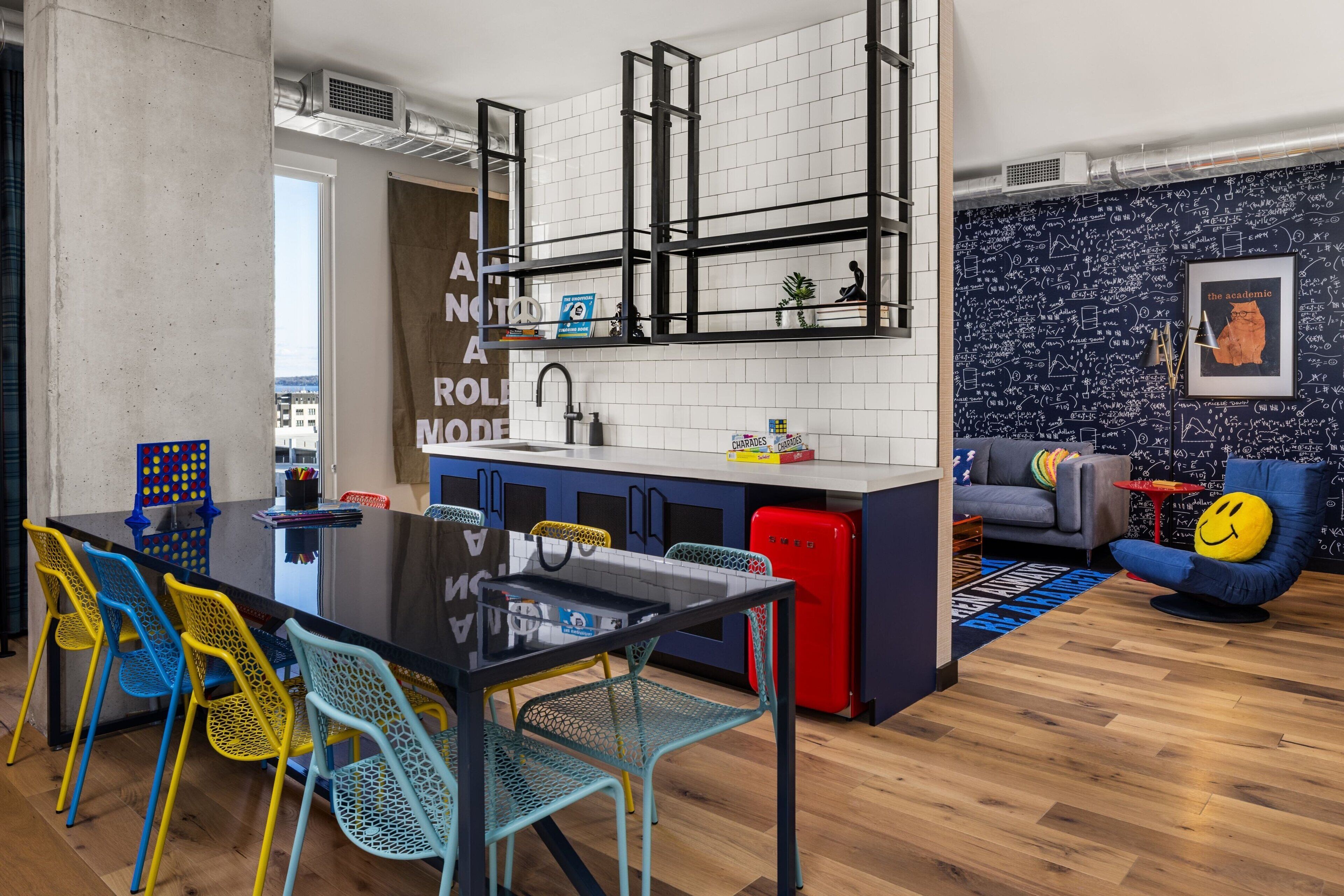 A modern kitchen with a black countertop, colorful chairs, and a red refrigerator.