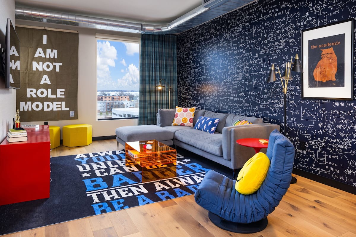 A modern living room with a grey sofa, yellow ottomans, a blue chair, and a black and white patterned rug.