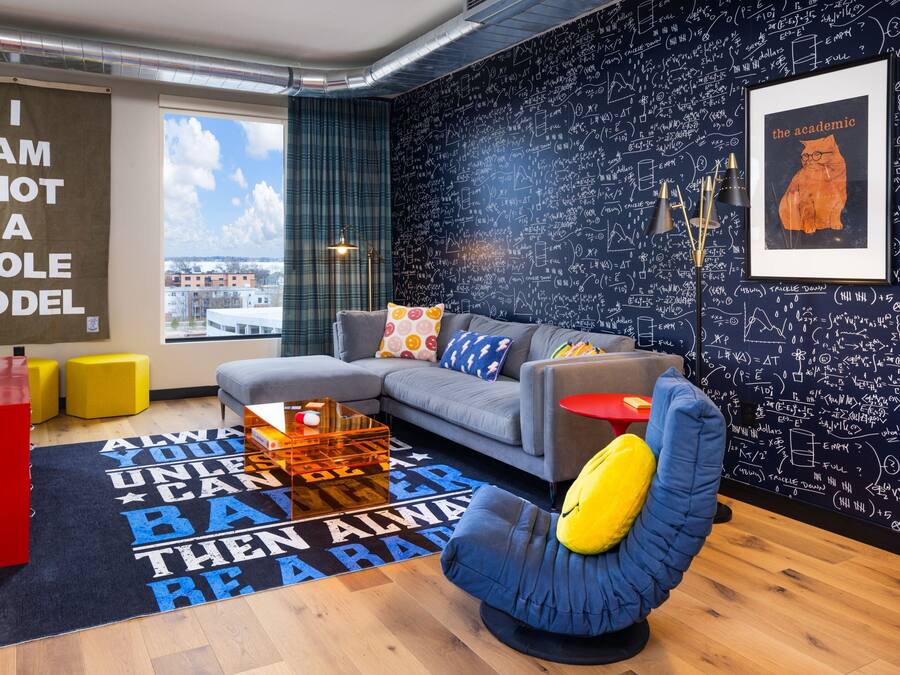 Un salon moderne avec un canapé gris, des poufs jaunes, un fauteuil bleu et un tapis à motifs noir et blanc.