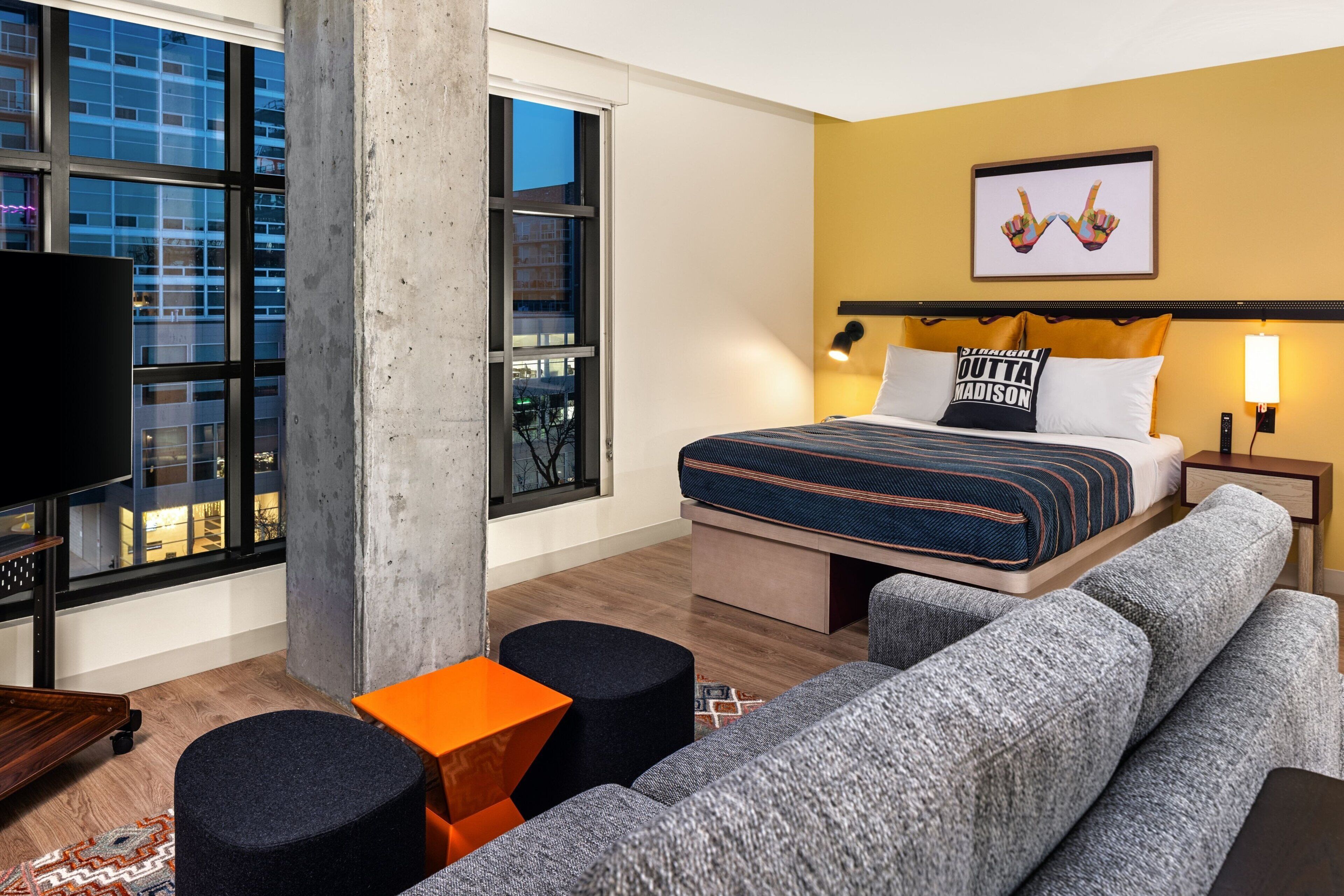 Una habitación de hotel moderna con una cama grande, un sofá, una mesita y un televisor.