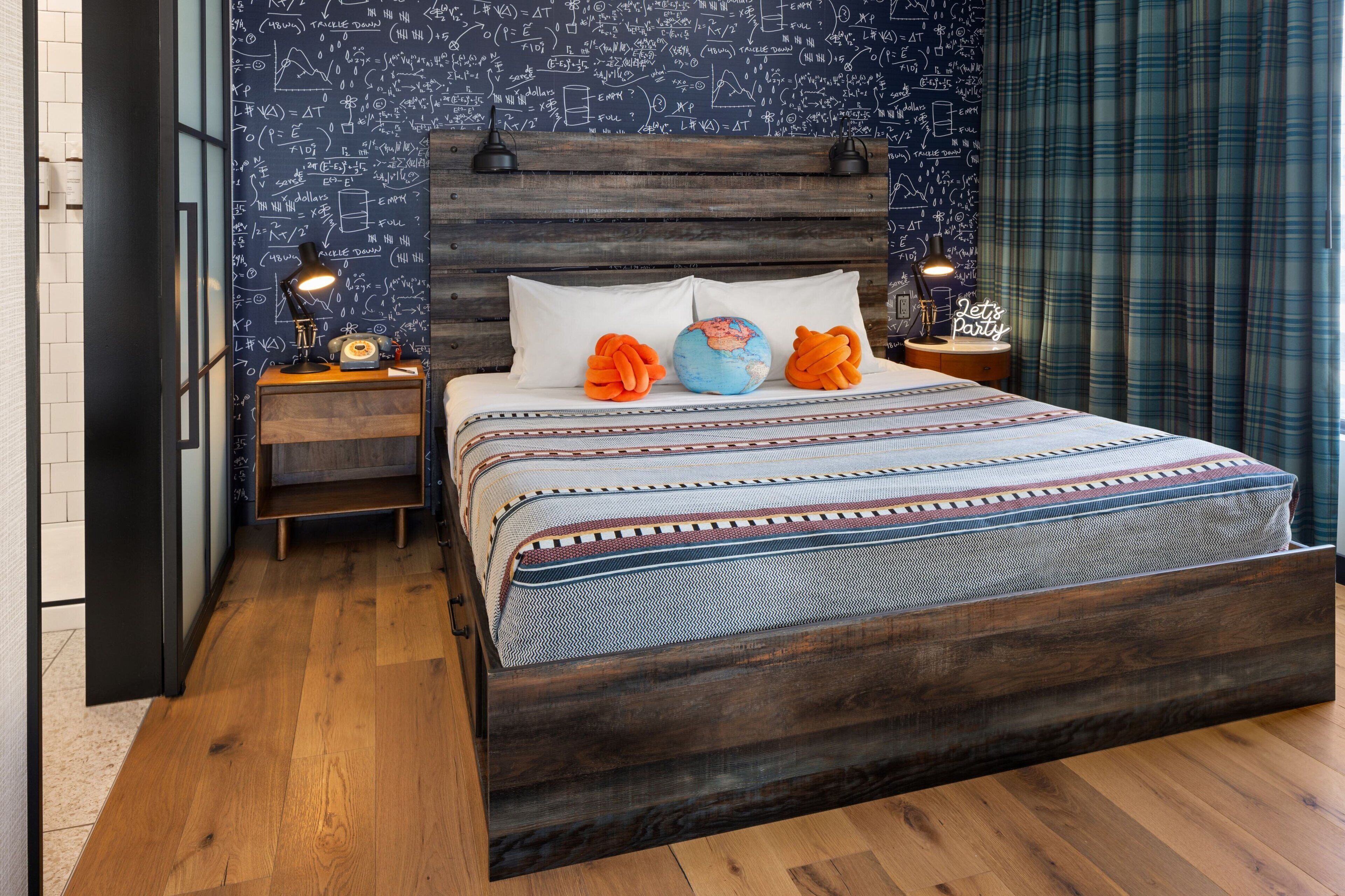 A bedroom with a wooden headboard, a bed with patterned bedding, two nightstands with lamps, and a wall with mathematical equations.