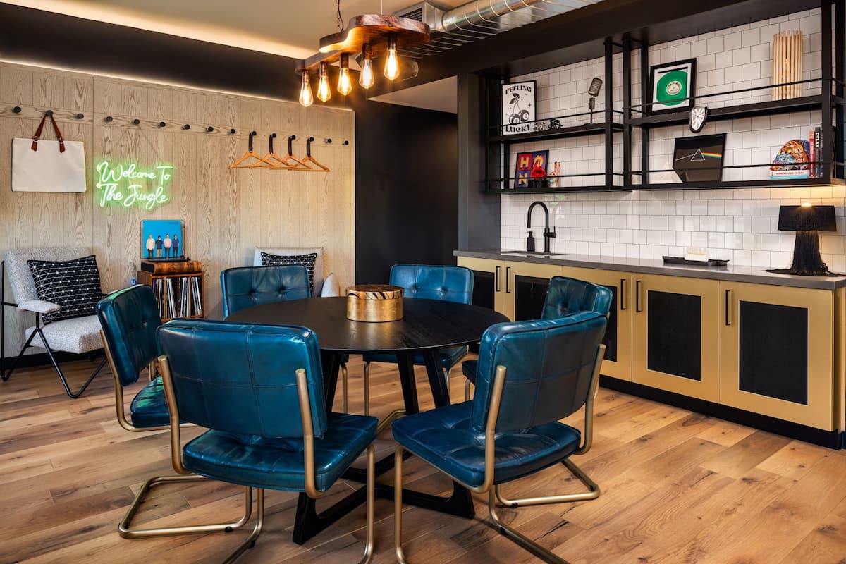 A modern kitchen with a round dining table, blue chairs, and a neon sign.