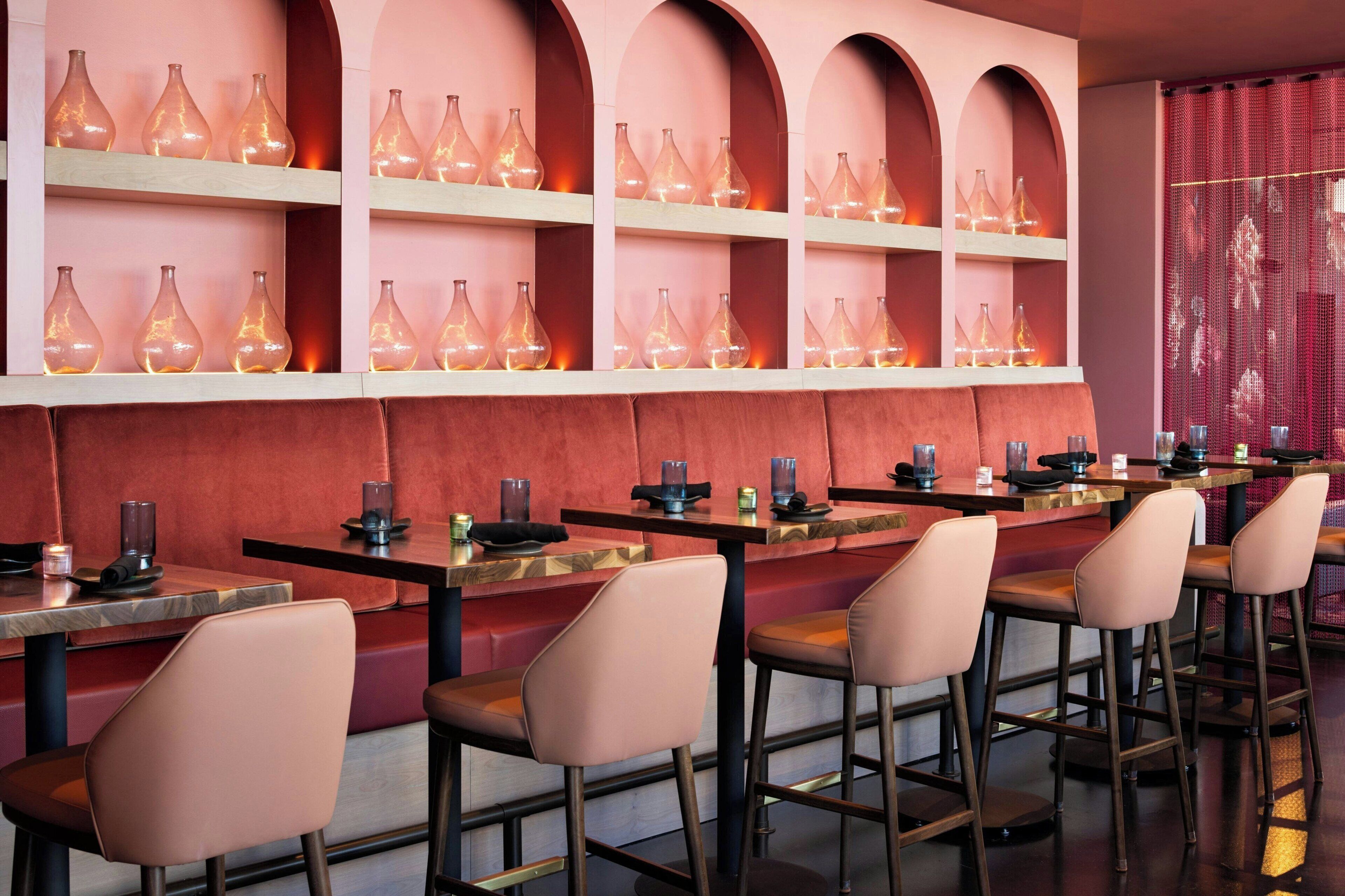 A restaurant interior with multiple tables and chairs, shelves with glassware, and a red wall with arches.