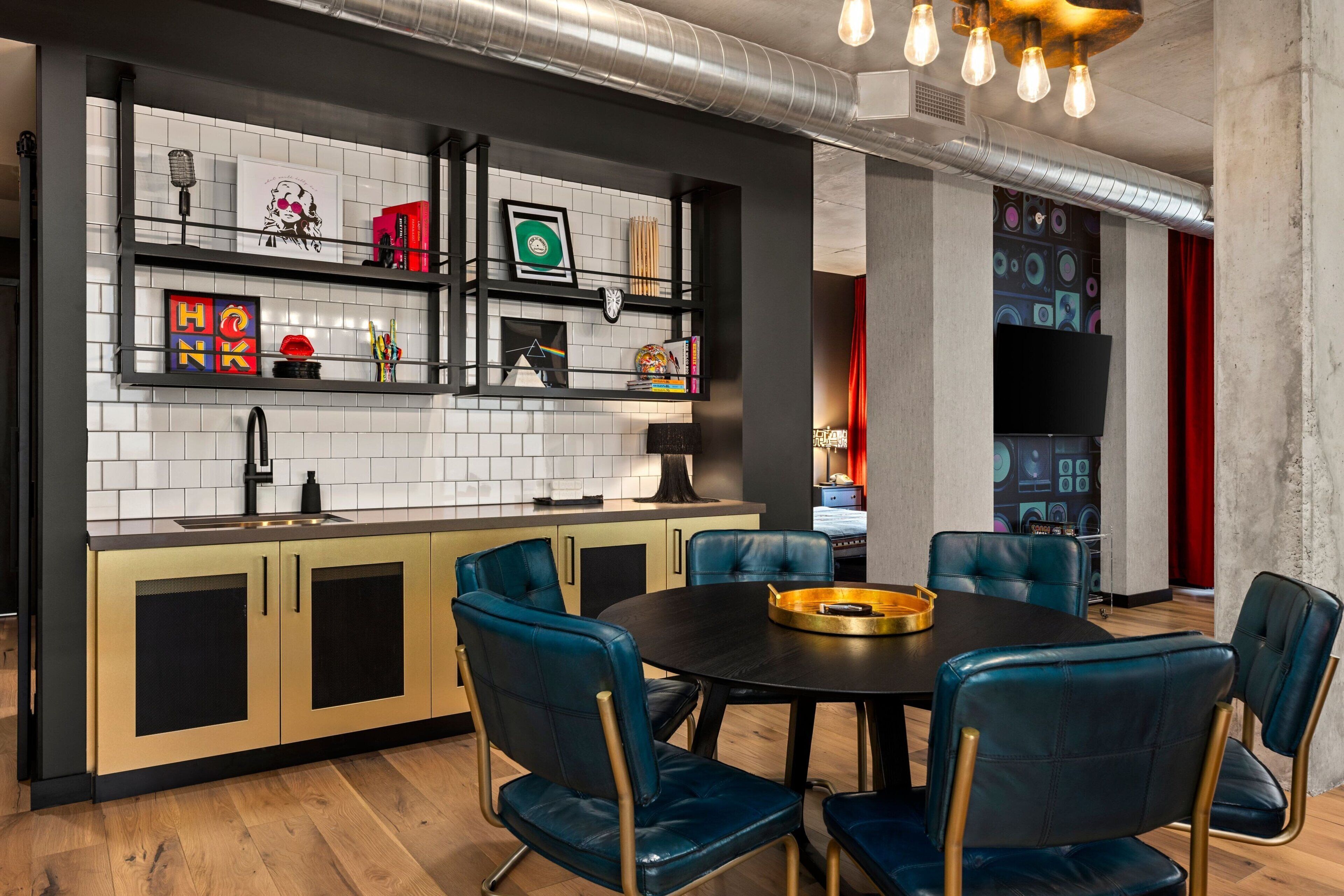 Una cocina moderna con encimera negra, salpicadero de azulejos blancos y sillas de cuero azul alrededor de una mesa de comedor negra.