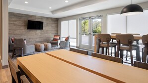 A modern hotel room with a wooden dining table, comfortable seating, a flat-screen TV mounted on a wooden wall, and large windows offering a view of the outdoors. - Candlewood Suites Chattanooga East Ridge by IHG (Chattanooga)