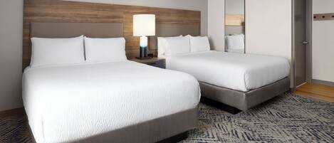 A hotel room with two beds, a nightstand with a lamp, a mirror, and a patterned carpet.