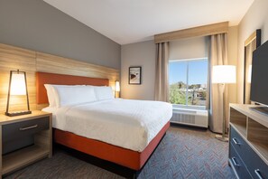 A hotel room with a large bed, a nightstand with a lamp, a dresser, and a large window offering a view of the outdoors.