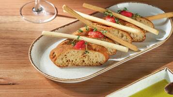 A plate of bread with strawberries and herbs, a glass of wine, and a small dish of green sauce on a wooden table.