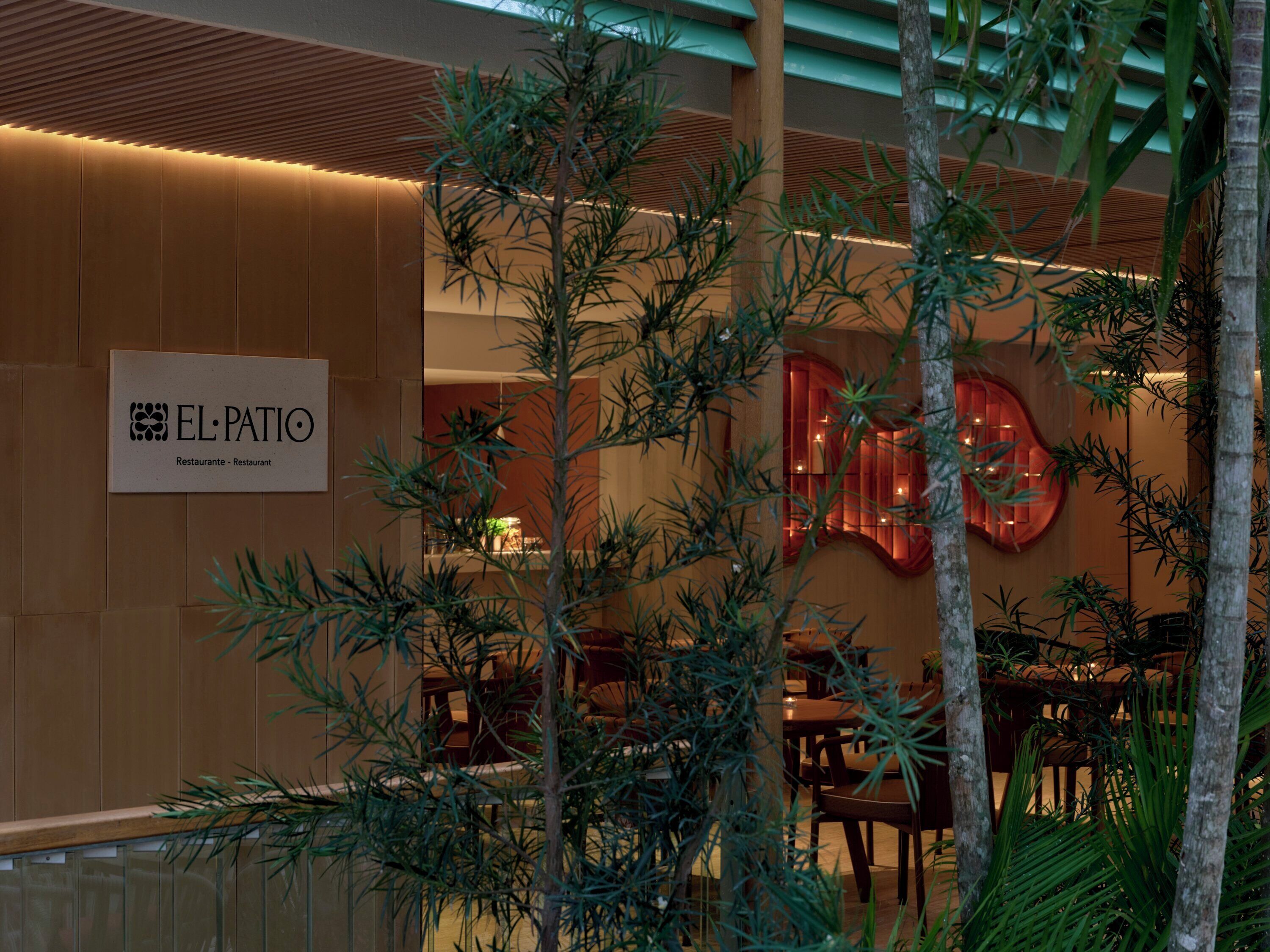 A restaurant interior with a sign reading "EL PATIO Restaurante - Restaurant" and a warm, modern design with wooden paneling and indoor plants.