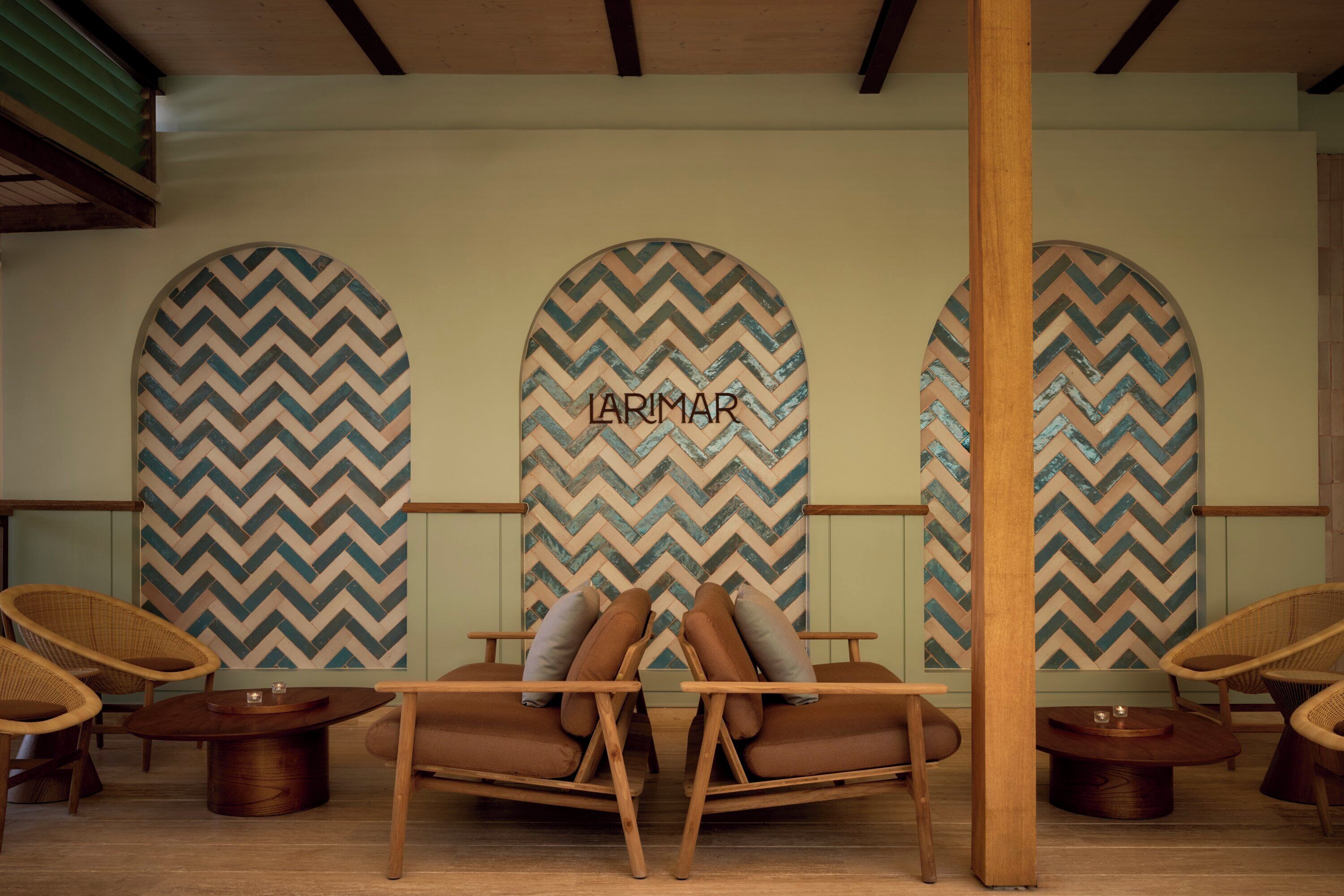 Una habitación con tres grandes decoraciones murales de diseño en zigzag, techo de madera y un área de descanso con dos sillones de cuero marrón y dos sillones de mimbre.