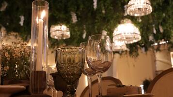 A table set with crystal glasses, a tall candle, and a decorative bowl, surrounded by greenery and hanging chandeliers.