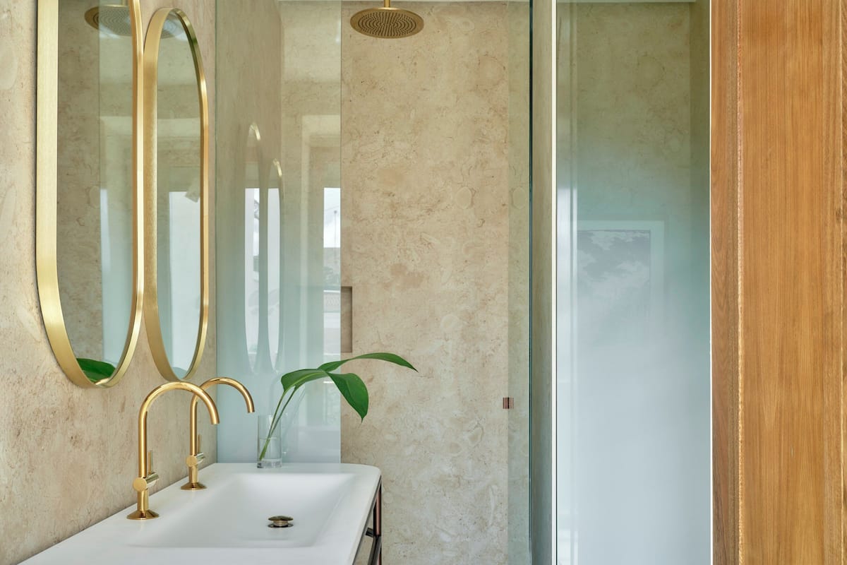 Ein Badezimmer mit einem weißen Waschbecken, goldenen Wasserhähnen und einem großen Spiegel.