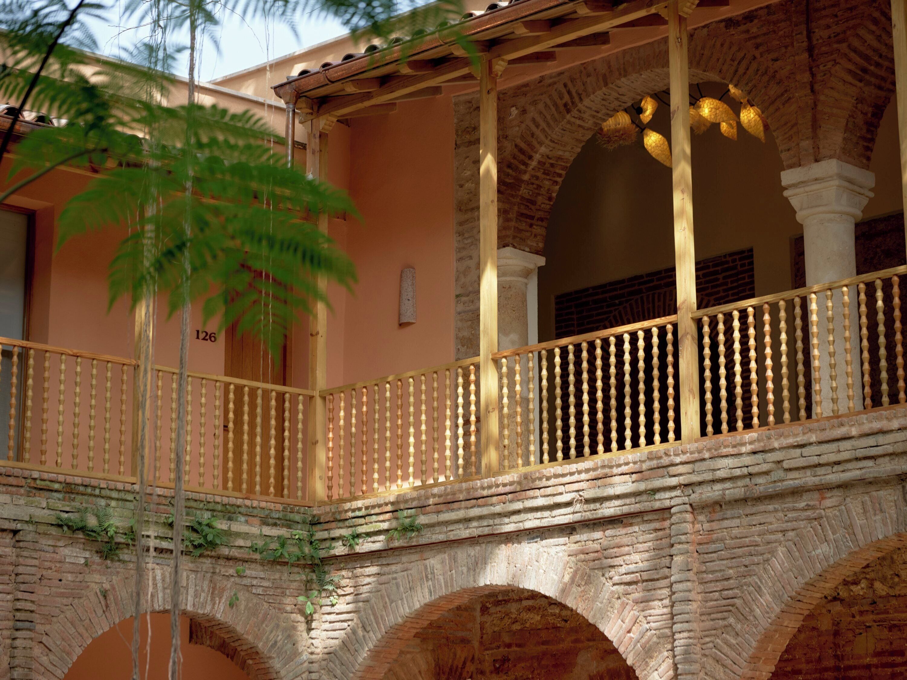 A balcony with a wooden railing, brick arches, and a palm tree.