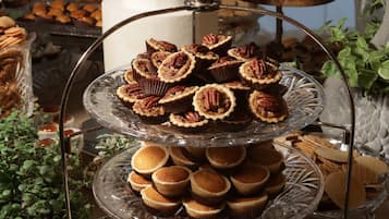 A multi-tiered dessert display with various pastries and a cake, surrounded by decorative plants and plates.