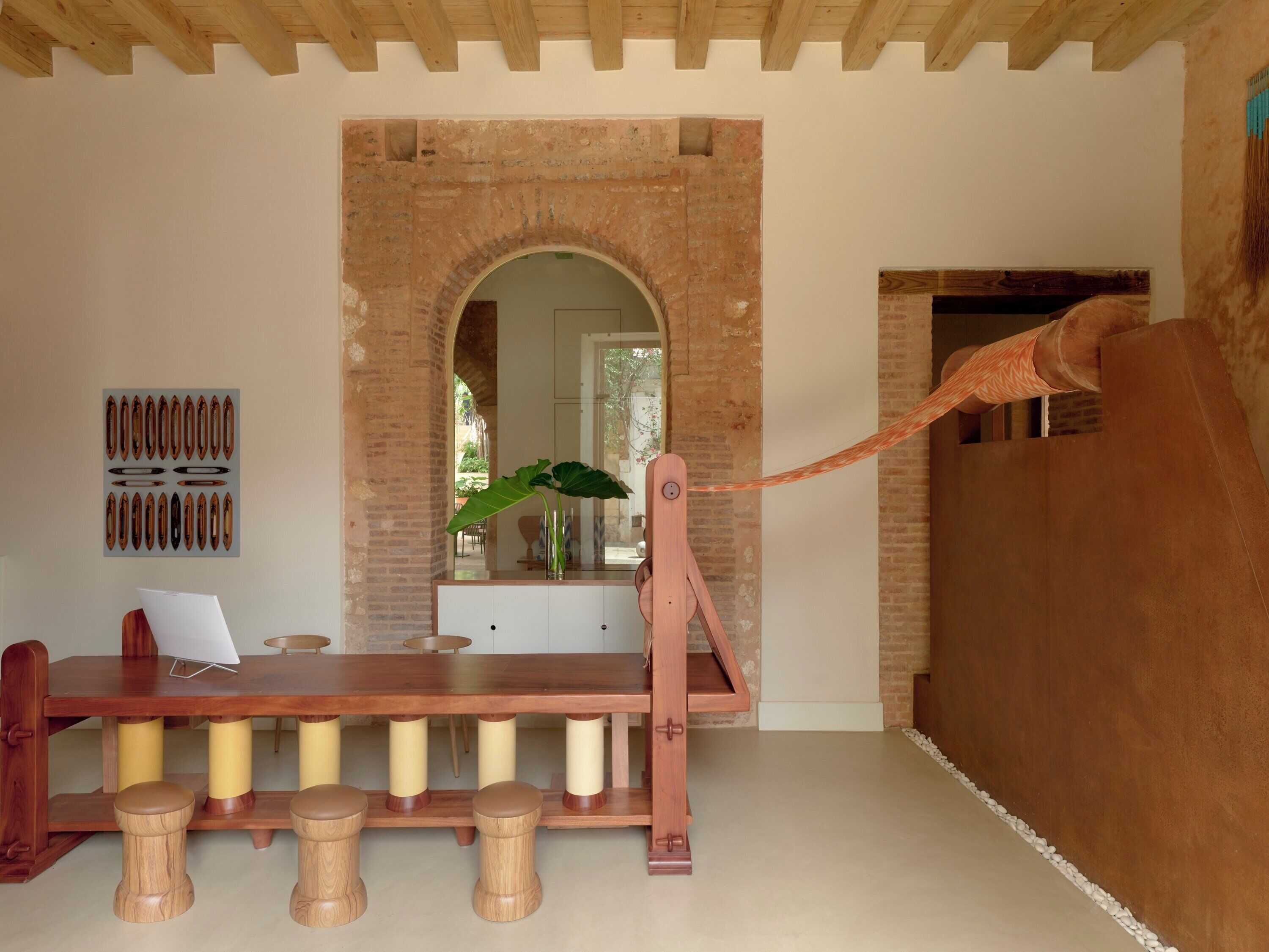 Een eethoek met een houten tafel, krukken, een bakstenen muur en een hangplant.